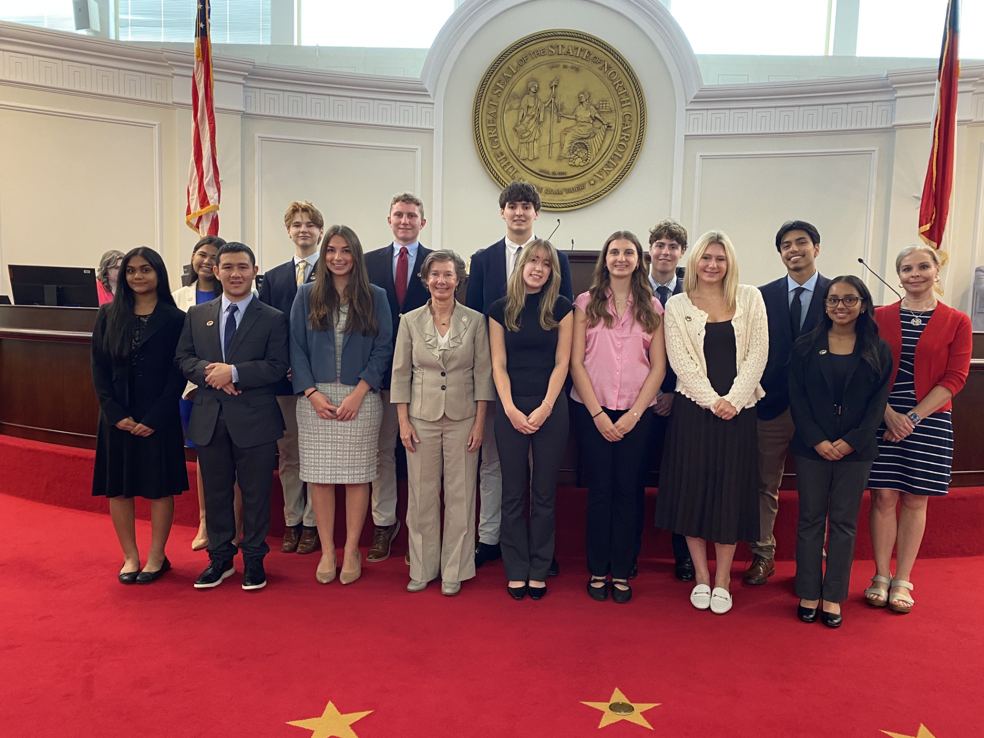 A group of Senate pages standing with a Senator in front of the Senate chamber dais.